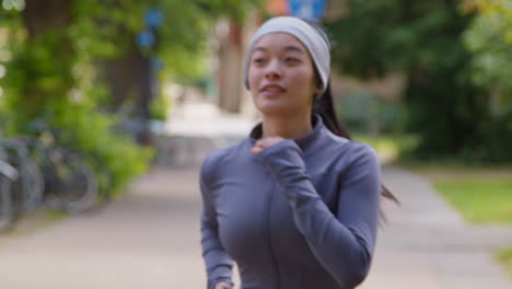 Close-Up-Of-Young-Woman-Exercising-Running-Through-City-Park-Wearing-Wireless-Earbuds-1