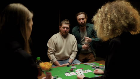 Rear-View-Of-Group-Of-Friends-Playing-Poker-Sitting-On-Chairs-At-A-Table