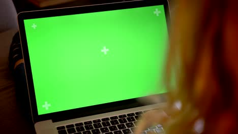 closeup back view shoot of adult caucasian attractive female typing on the laptop with green chroma screen while sitting on the couch indoors