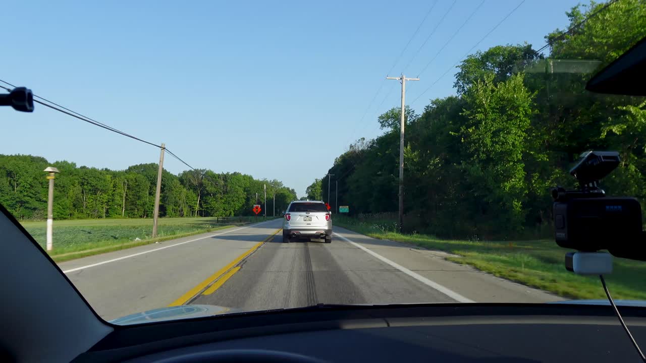 A car drives down a rural road with traffic signs and trees lining the sides. Perfect for travel, transportation, or countryside footage.