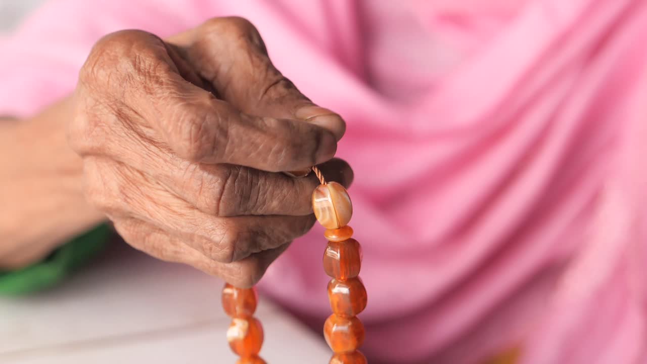 mujer anciana orando con cuentas de oración