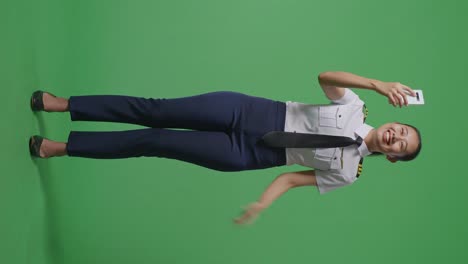 cuerpo lleno de mujer asiática piloto agitando la mano teniendo una llamada de video en el teléfono inteligente mientras estaba de pie en la pantalla verde estudio de fondo