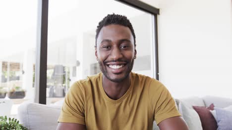 portrait of happy african american man making video call, talking in living room, in slow motion