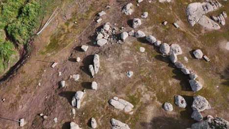 Vuelo-Inverso-Con-Un-Dron-Sobre-Un-Cromlech-De-Piedra-De-Granito-Sobre-Un-Suelo-Marrón-Cercado-Con-Una-Cuerda-Y-Dejando-En-El-Lado-Izquierdo-El-Curso-De-Un-Arroyo-Con-Vegetación-En-Toledo,-España