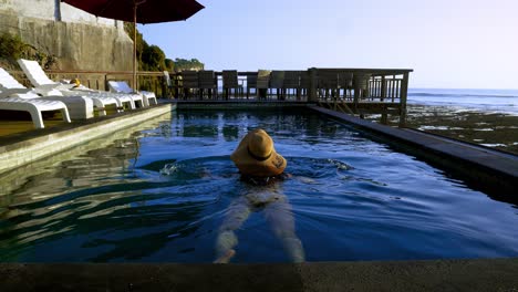 Zeitlupenaufnahme-Eines-Schwimmenden-Modells-Im-Infinity-Pool-Auf-Bali-Mit-Blick-Auf-Den-Strand-Von-Saluban-Bei-Ebbe-An-Einem-Sonnigen-Tag