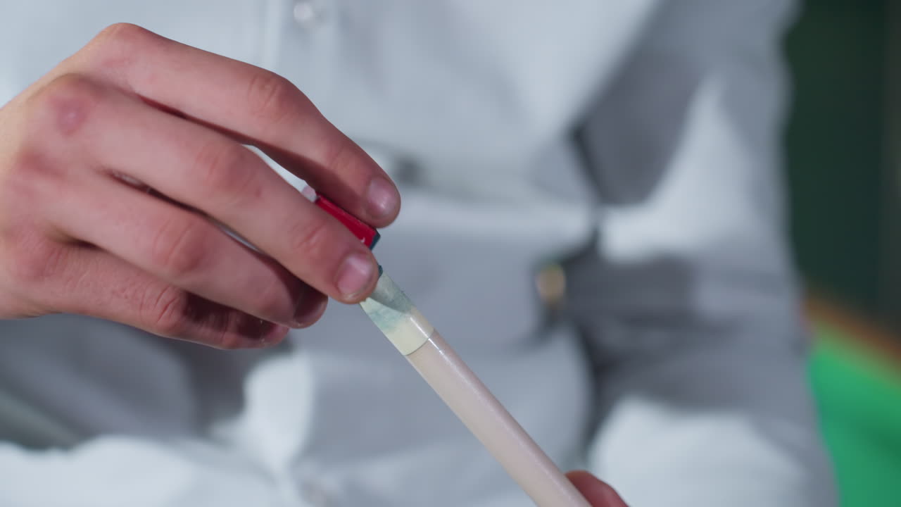 toma de primer plano de la mano del jugador en camisa blanca aplicando cuidadosamente tiza roja y azul al palo de señal antes del juego de billar. el agarre enfocado destaca la precisión, la preparación y la habilidad en el billar