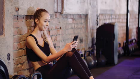 Beautiful-Female-Athlete-Text-Messaging-Through-Mobile-Phone-During-Break-At-Health-Studio-3