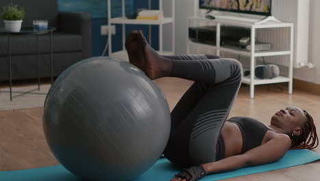Woman-with-black-skin-training-abs-on-swiss-ball-in-living-room