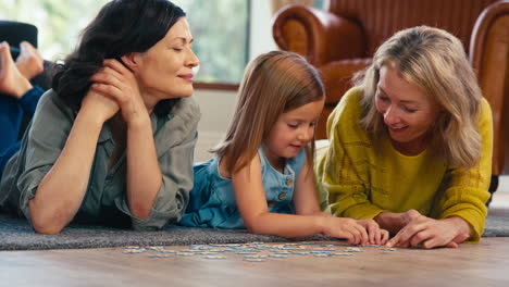 Same-Sex-Family-With-Two-Mature-Mums-And-Daughter-Lying-On-Floor-Doing-Jigsaw-Puzzle-At-Home