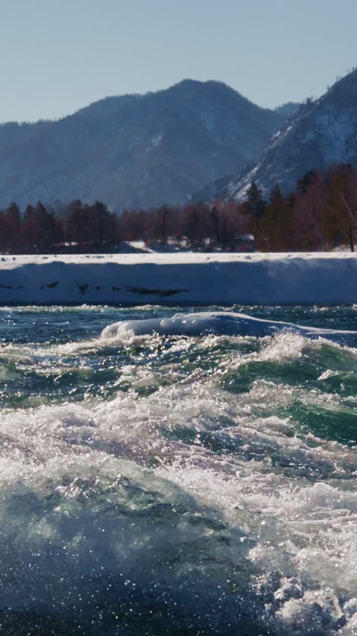 Raging river flows swiftly through snowy mountains in winter landscape