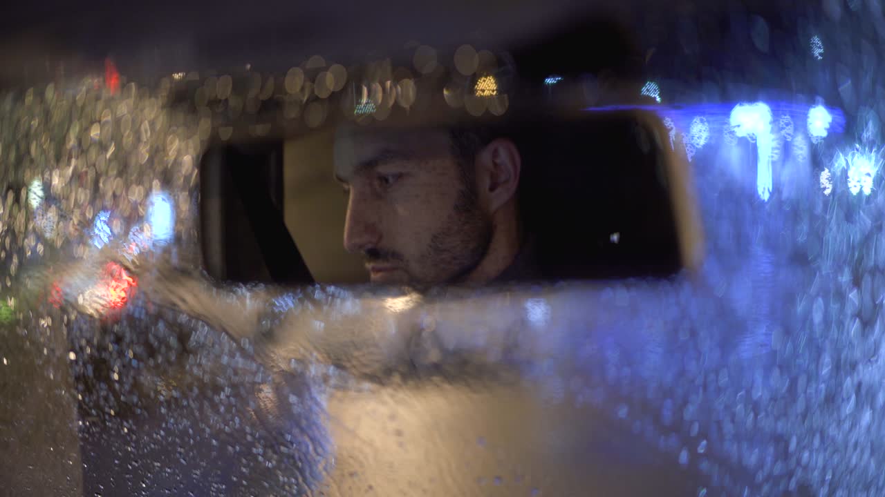 매력적인 남자가 비가 오는 밤에 차에 앉아 있습니다.