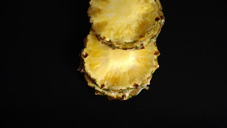 rebanadas redondas de piña fresca caen sobre las salpicaduras de agua.