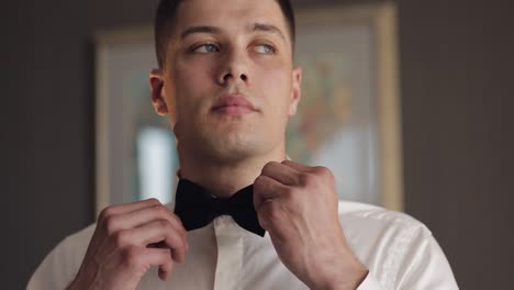 Groom-adjusts-bow-tie,-preparing-to-go-to-the-bride,-businessman-in-white-shirt,-wedding-day