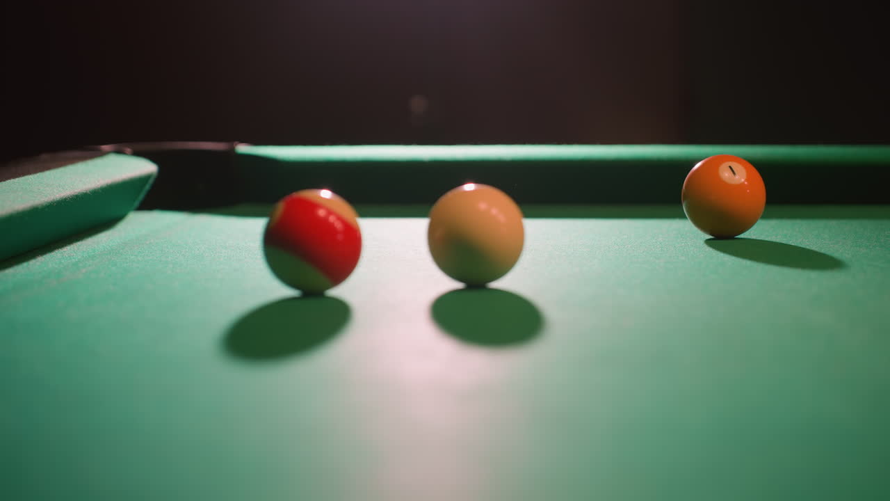 Une boule de billard blanche roule sur une table de billard verte après avoir frappé une boule verte et l’avoir fait tomber dans une poche. Un éclairage spectaculaire met en évidence l’intensité de ce moment stratégique dans une partie compétitive.