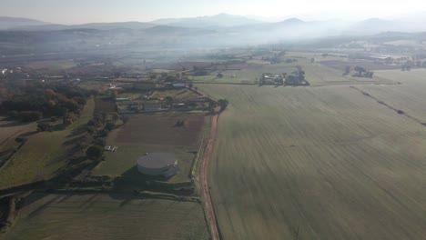 Luftvideo-Eines-Neu-Gesäten-Feldes-Mit-Einer-Unbefestigten-Straße-In-Der-Mitte-Und-Bergen-Im-Hintergrund-Grünes-Kultiviertes-Feld-Von-Llagostera-Gerona