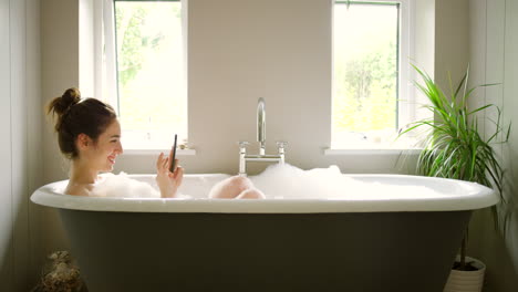 woman relaxing in a bubble bath with phone