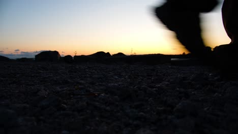 silueta de las piernas de un excursionista caminando por una playa rocosa al atardecer