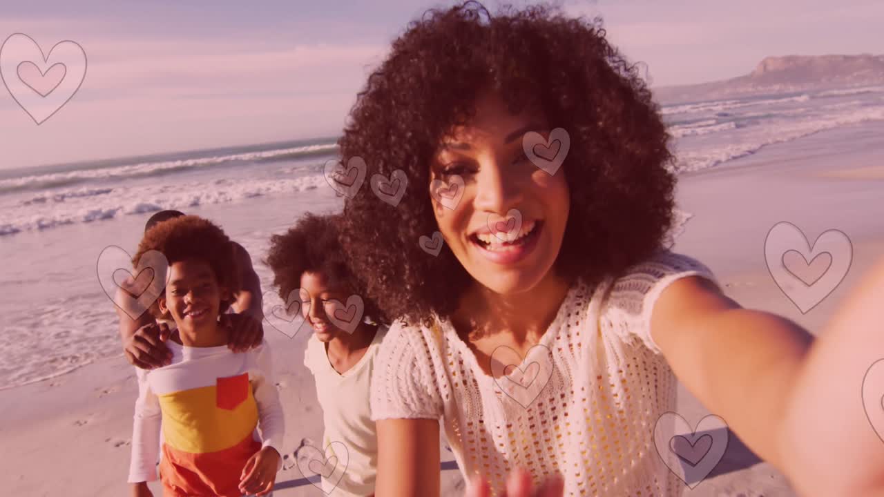 Animazione della scritta Hohoho e cuori su una famiglia afroamericana felice in spiaggia durante il periodo natalizio