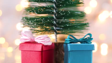 mini árbol de navidad con luces parpadeantes detrás y dos regalos debajo del árbol