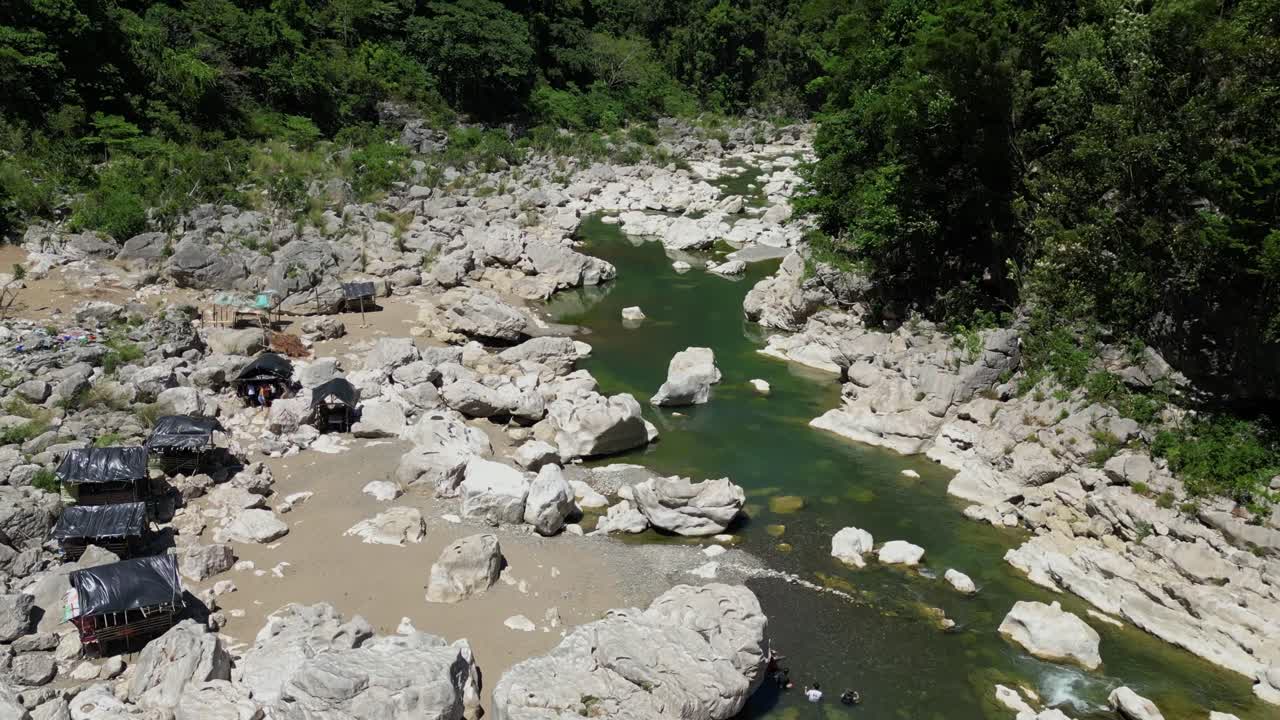 Forward shot reveals cottages along the riverbanks, showing the river and lush nature surrounding Tinipak River, Philippines