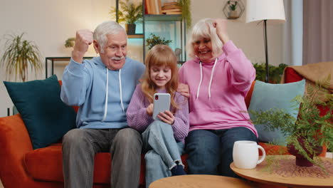 child girl granddaughter grandfather grandmother using smartphone celebrating game win victory