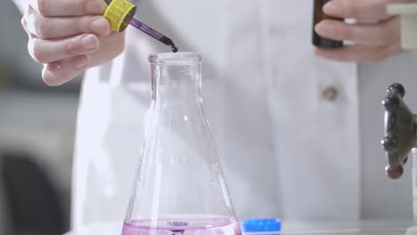 scientist adding liquid to flask in lab