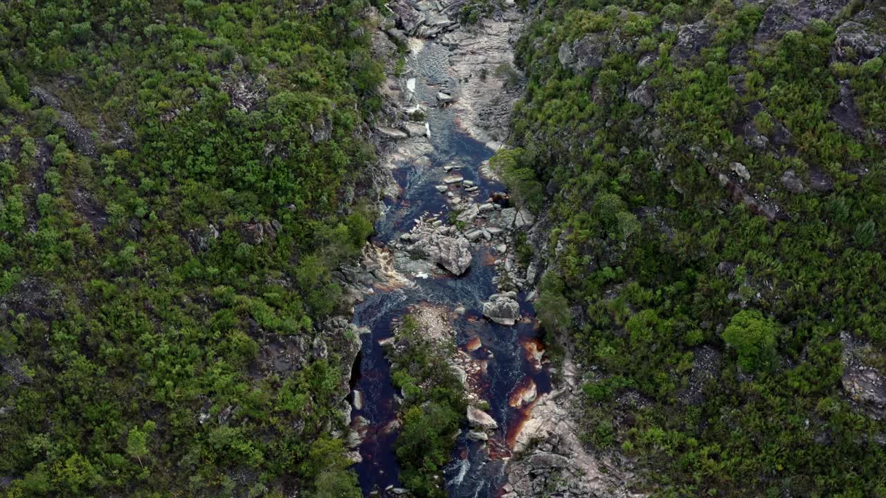 un dron aéreo de arriba hacia abajo que pasa por encima de un increíblemente impresionante río rocoso y ventoso que conduce al pozo del diablo en una caminata en el hermoso parque nacional chapada diamantina en el noreste de brasil