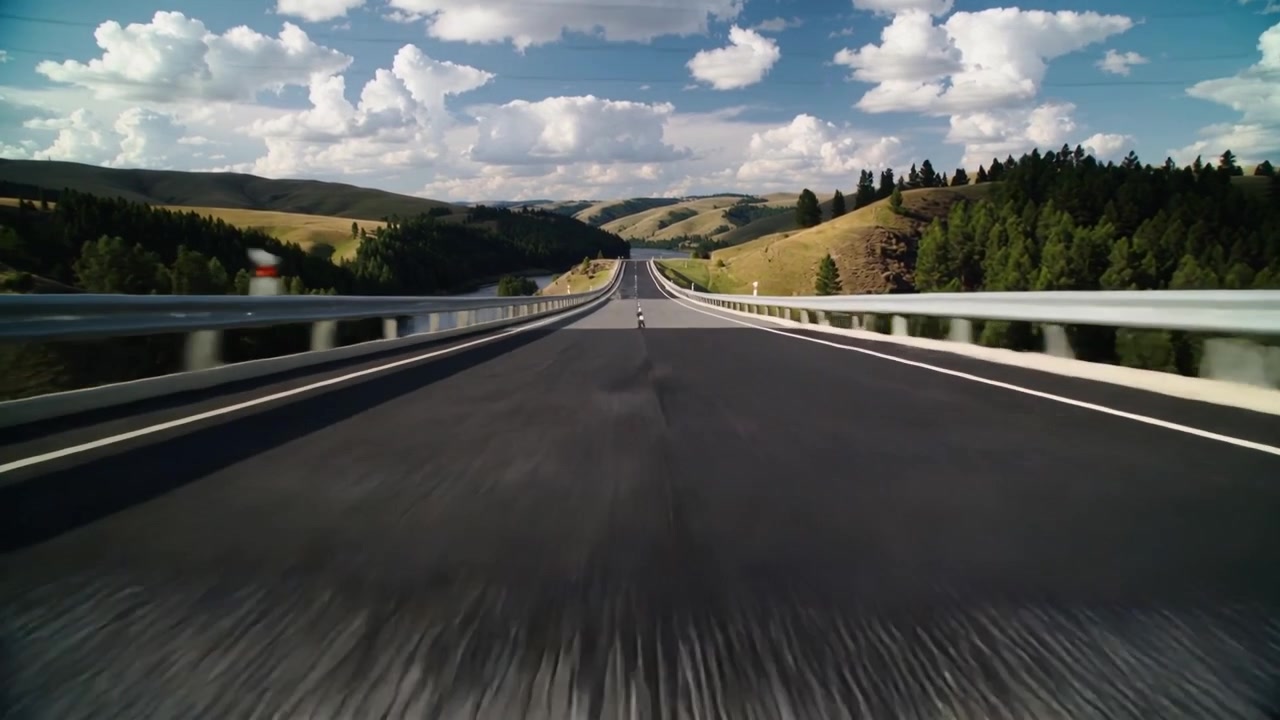 Telecamera che avanza attraversando un ponte a due corsie, mostrando la linea bianca centrale, un dissuasore e il piano stradale lucido