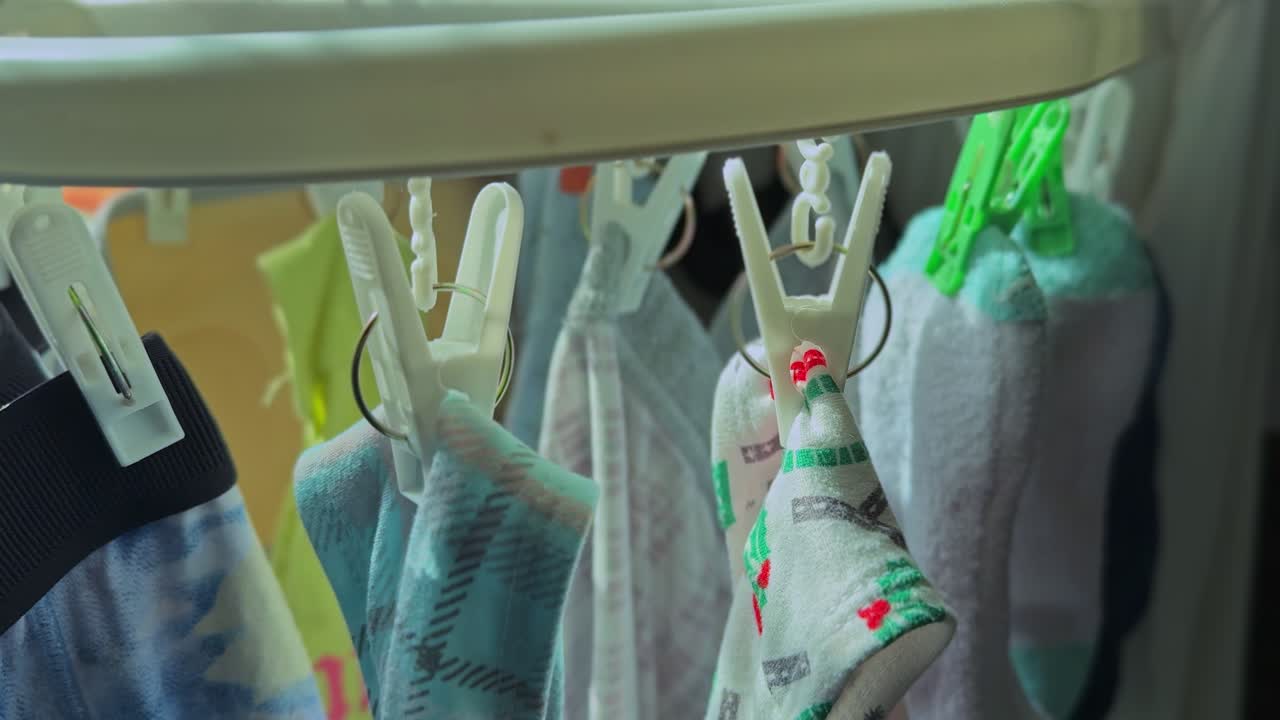 Detailed close-up of socks and small garments clipped to a circular drying rack beside a sunlit apartment window, showing an indoor household laundry routine in soft natural daylight
