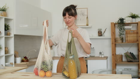 mujer descargando comestibles de bolsas de red en la cocina