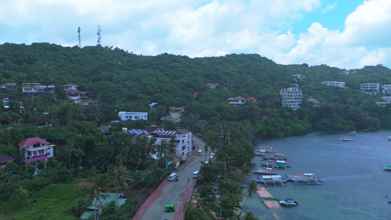 Rainy day aerial of Boracay, Philippines showing turquoise waters, fishing boats, palm-lined road, and hillside villas. Ideal for travel, weather, and cinematic projects