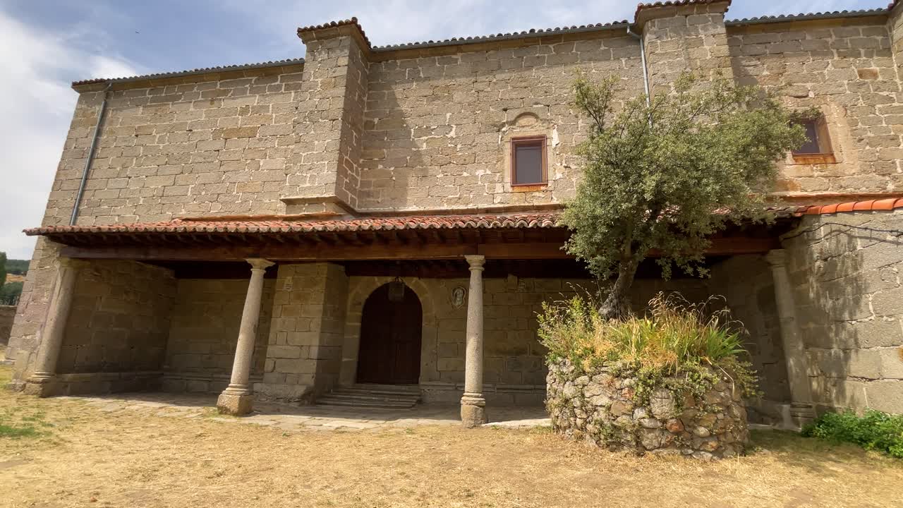 impressive facade of the medieval-style religious sanctuary all made of granite stone, we appreciate its entrance with its wooden door, two columns and a large planter with an oak tree, in slow motion