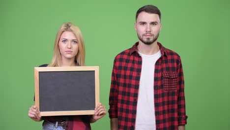 young couple holding blackboard and pointing finger up together