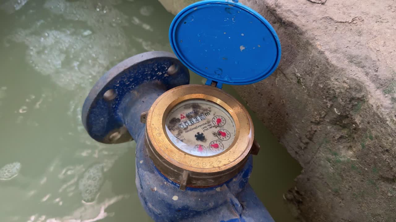 Analog water meter with brass frame and blue frame with running rotating water flow measuring wheel to measure the amount of wastewater flowing into the holding pond