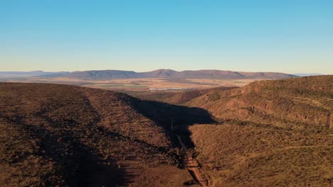 Majestic-mountain-pass-with-stunning-rocky-landscapes-and-lush-green-fields-in-the-distance---Drone-high-up