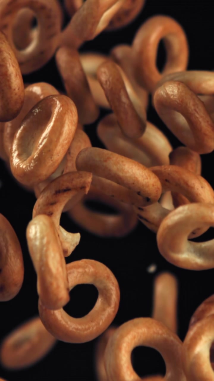 Deliziosi bagel dorati che cadono al rallentatore su sfondo nero