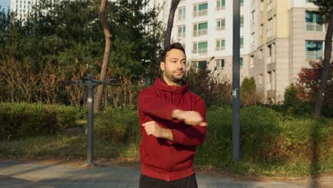 hombre barbudo estirando los brazos en un parque de apartamentos al aire libre antes de una carrera o entrenamiento de maratón