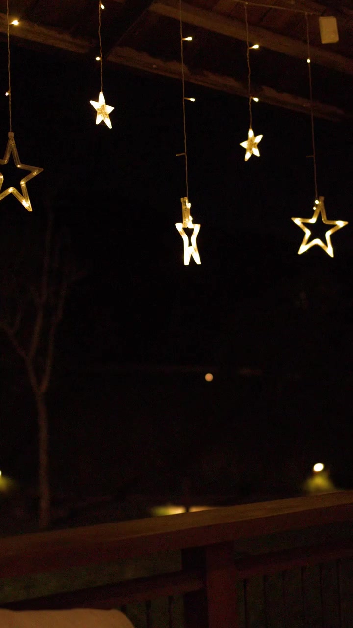 Warm star-shaped string lights hang from a wooden terrace roof against a dark night sky