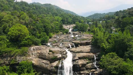 aerial drone shot of a picturesque waterfall flowing through munnar’s scenic landscape