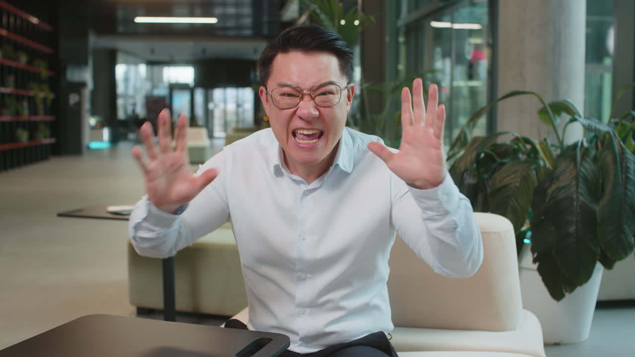 Angry mature boss arguing over video call looking at camera sitting at modern workplace in office