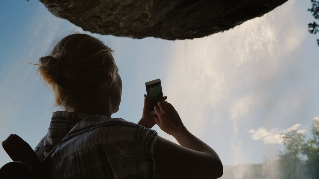steinsdalsfossen 폭포 아래 서 있는 여성이 그 위의 사진을 찍고 장엄한 바위를 걸고 있습니다.