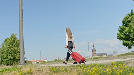 Frau-Geht-Im-Park-Spazieren-Und-Zieht-Dabei-Eine-Gepäcktasche-Mit-Rollen-Entlang,-Kamerafahrt-Aus-Der-Hand