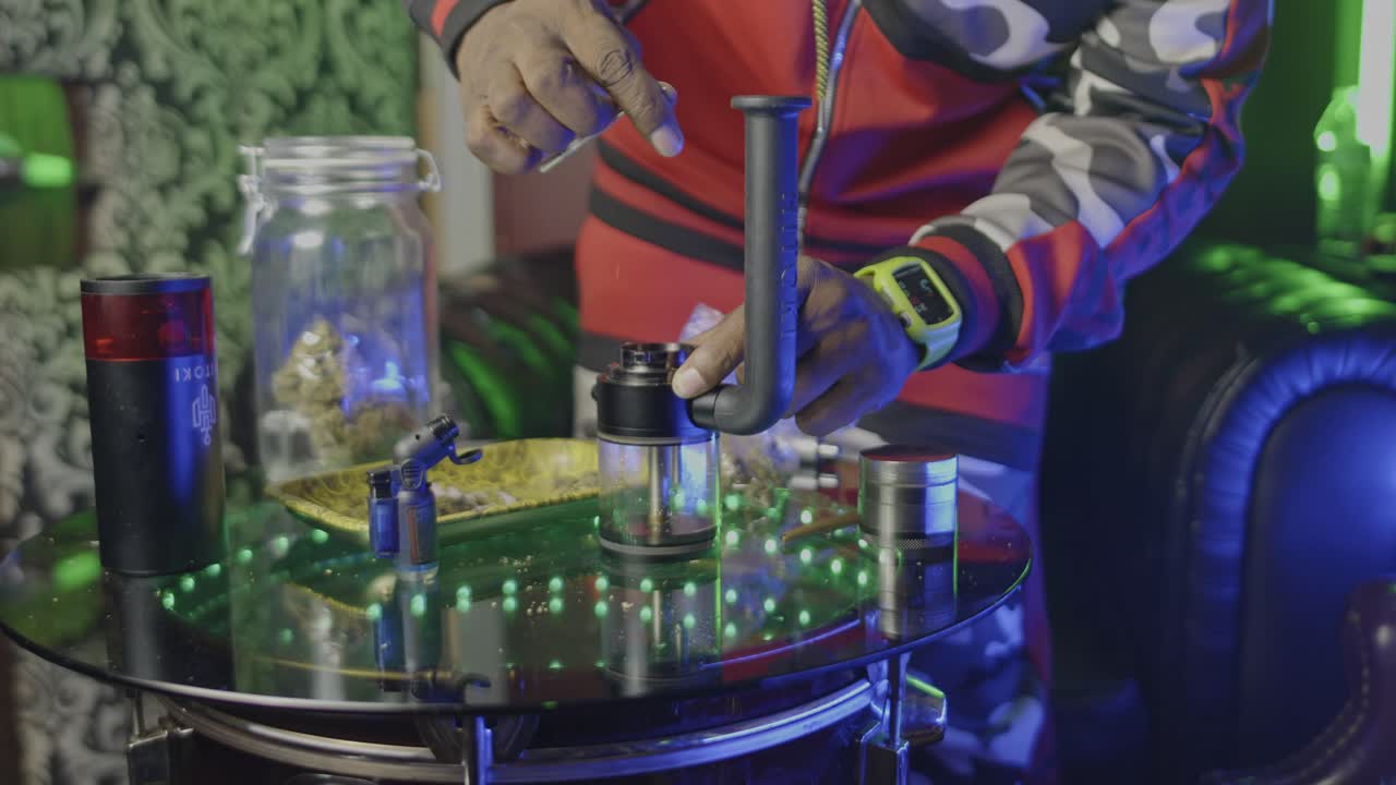 un hombre negro empaca el tazón de un bong de agua electrónico con marihuana preparándose para fumar la hierba