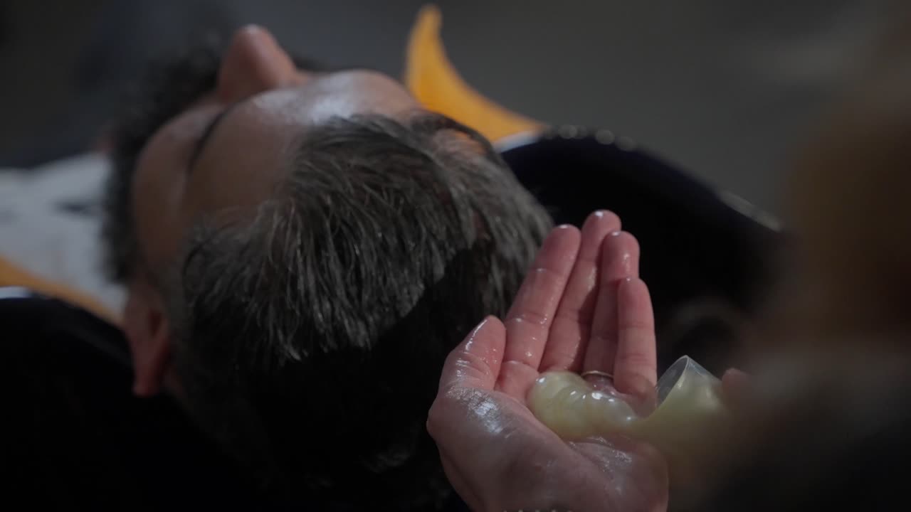 여성 이발사 가  ⁇ 푸 와 물 로 머리 를 부드럽게  ⁇ 는 의자 에서 헤어 살롱 에 앉아 있는 남자 의 클로즈업 슬로 모션  ⁇