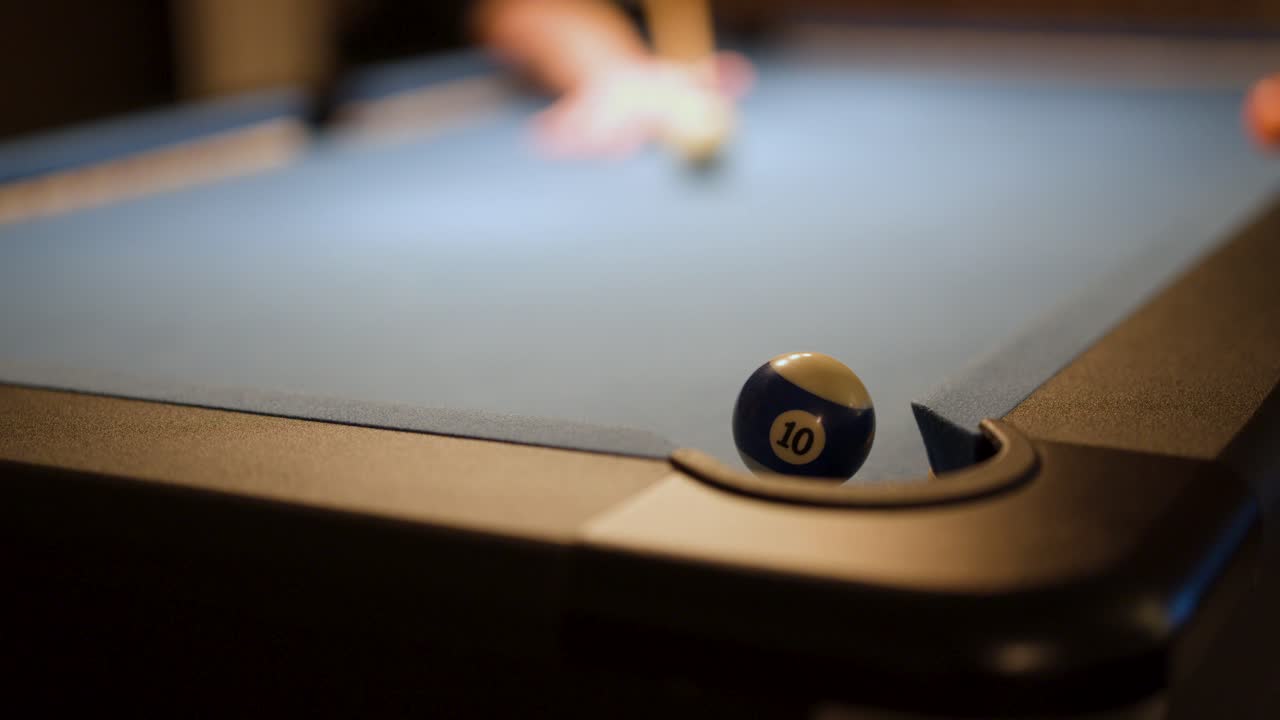 A pool player sinks the ten ball into a corner pocket under warm, low lighting