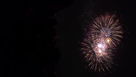 Vertical-view-of-fireworks-exploding-in-slow-motion-with-silhouetted-crowds