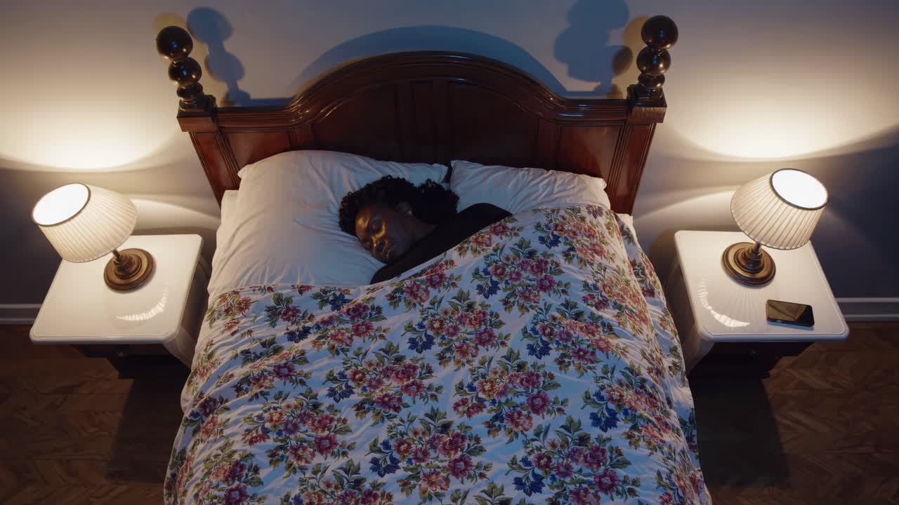 Overhead shot of a person sleeping in a cozy, warmly lit bedroom with floral bedding