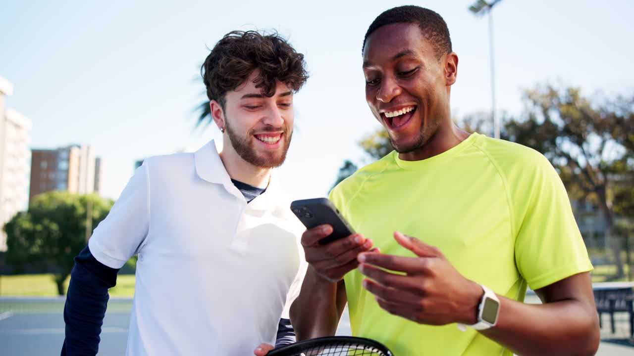 Two Young Men Smiling While Looking at Smartphone Outdoors
