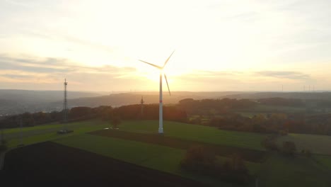 Vuelo-De-Drones-Sobre-Campos-Verdes-Con-Turbinas-De-Viento-Hacia-El-Amanecer