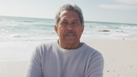 Porträt-Eines-Hispanischen-älteren-Mannes,-Der-Am-Strand-Steht-Und-In-Die-Kamera-Blickt